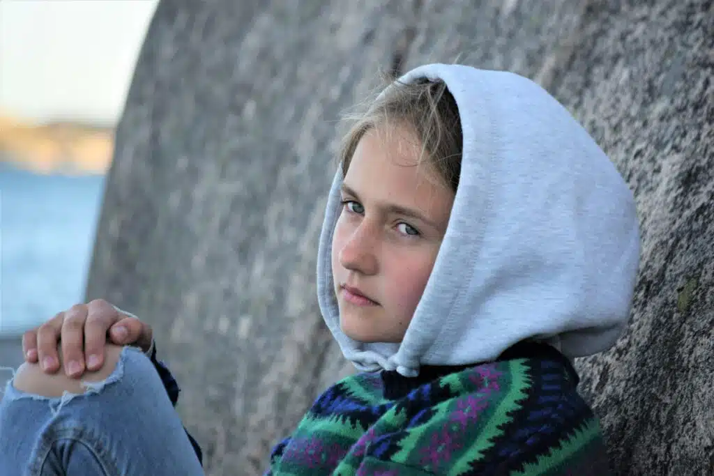 Jente med hette på hodet som sitter inntil fjellvegg